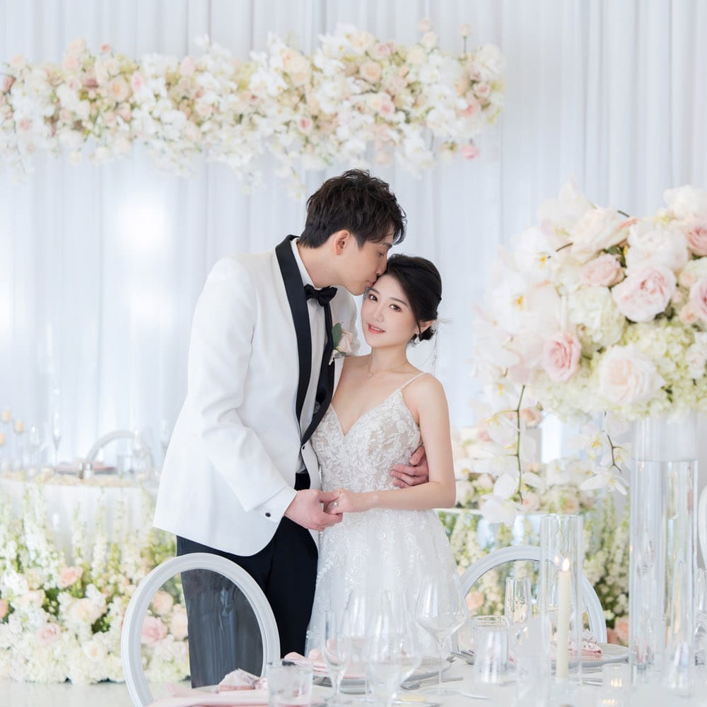 Bride and groom share a romantic moment at their reception, surrounded by soft white and blush floral arrangements at their oceanfront wedding at Hyatt Regency Huntington Beach