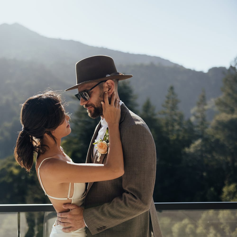 Bride and groom embrace in their wedding attire in front of a mountainous landscape at a private residence in San Francisco