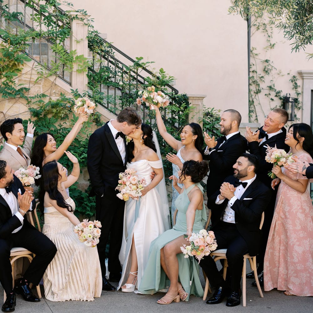 Bride and groom share a kiss while their wedding party cheers them on