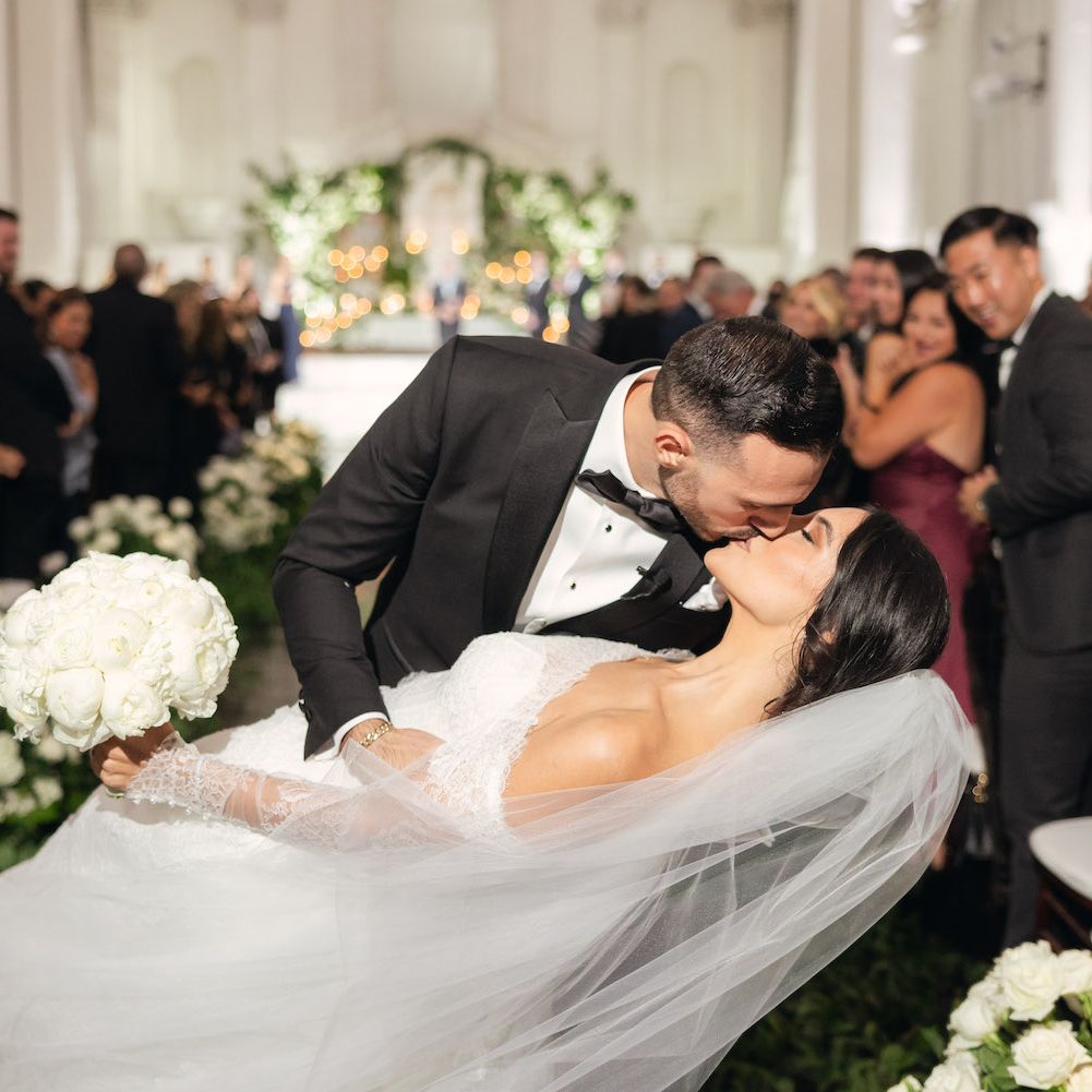 A gorgeous couple in classic wedding attire with long veil at elegant greenery altar with Armenian touches