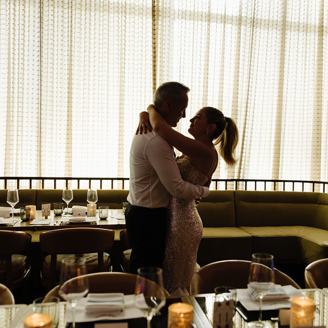 Kate and Tim embrace amidst reception scene at Mara