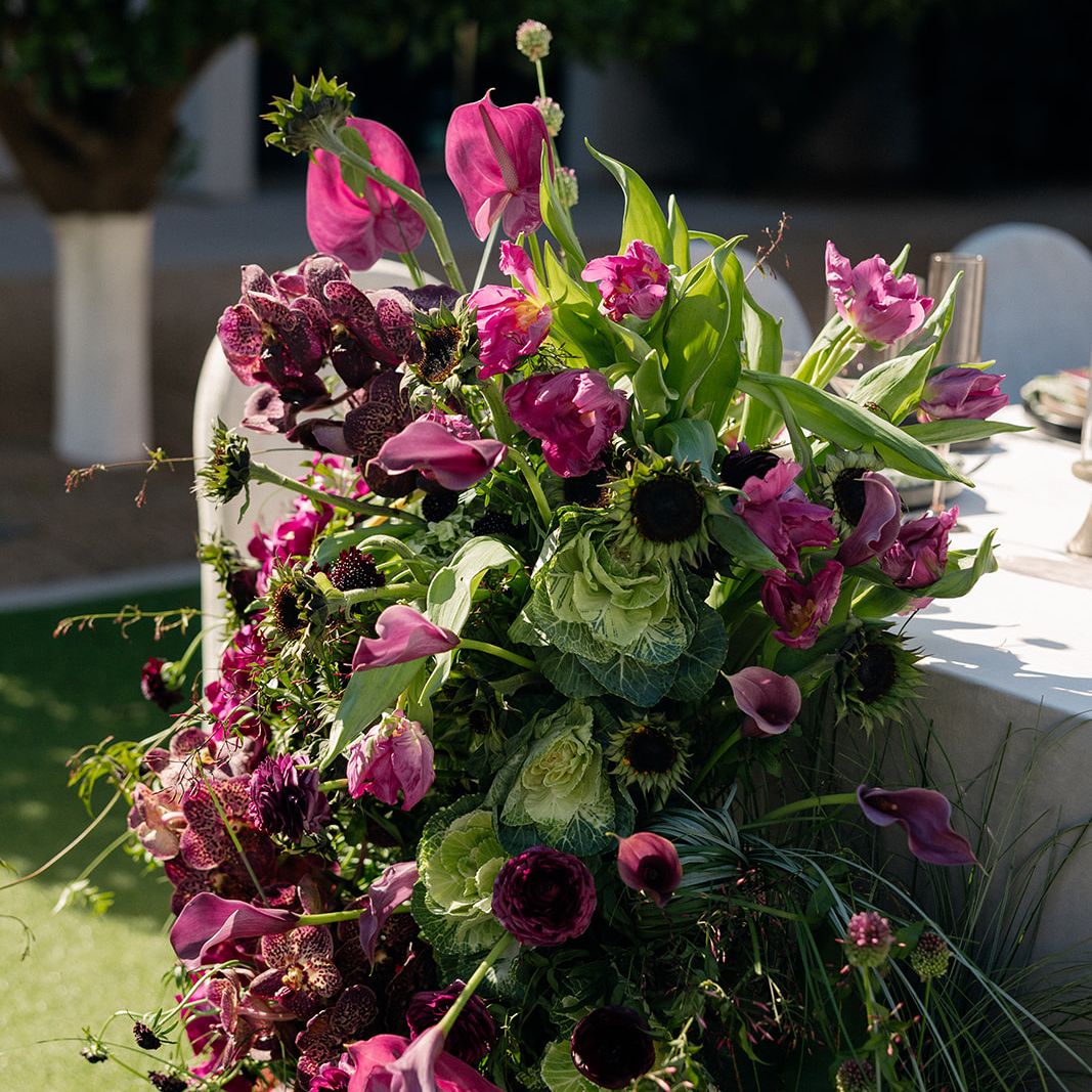 Close-up of a vibrant wedding floral installation with pink anthuriums, purple blooms, ornamental cabbage and textured greenery