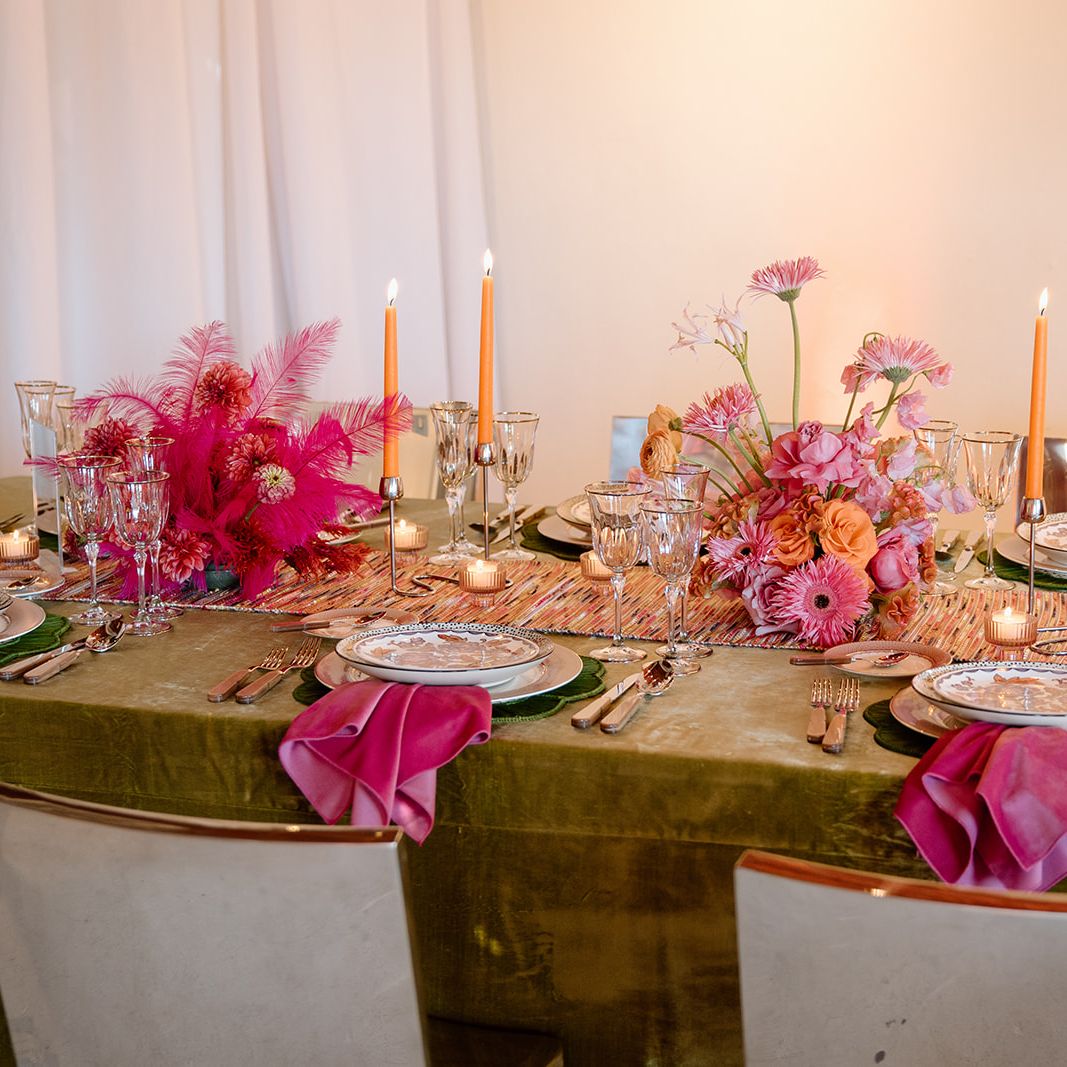 Colorful maximalist wedding tablescape with pink and orange floral centerpieces, green velvet linens and orange taper candles