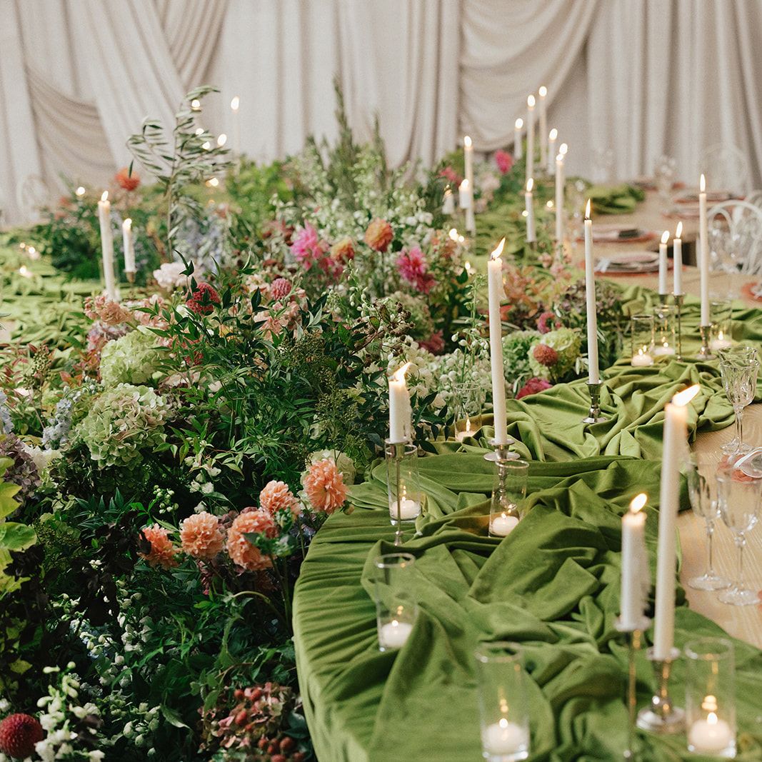 Serpentine tablescape featuring vivid décor, bright florals and romantic candlelight set against a draped background in editorial at The Woodland