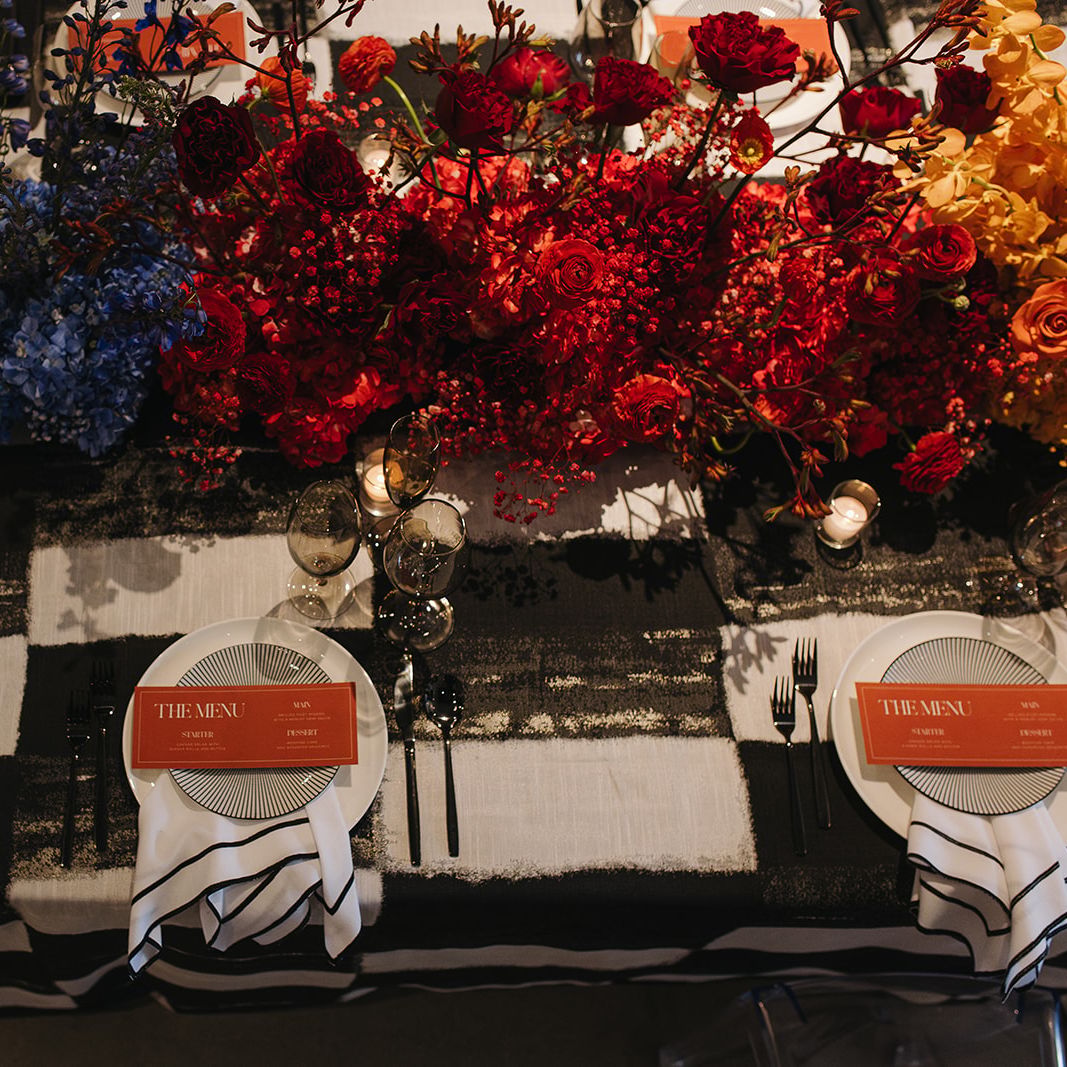 Maximalist tablescape featuring black and white checkered tablecloth and ombre rainbow florals
