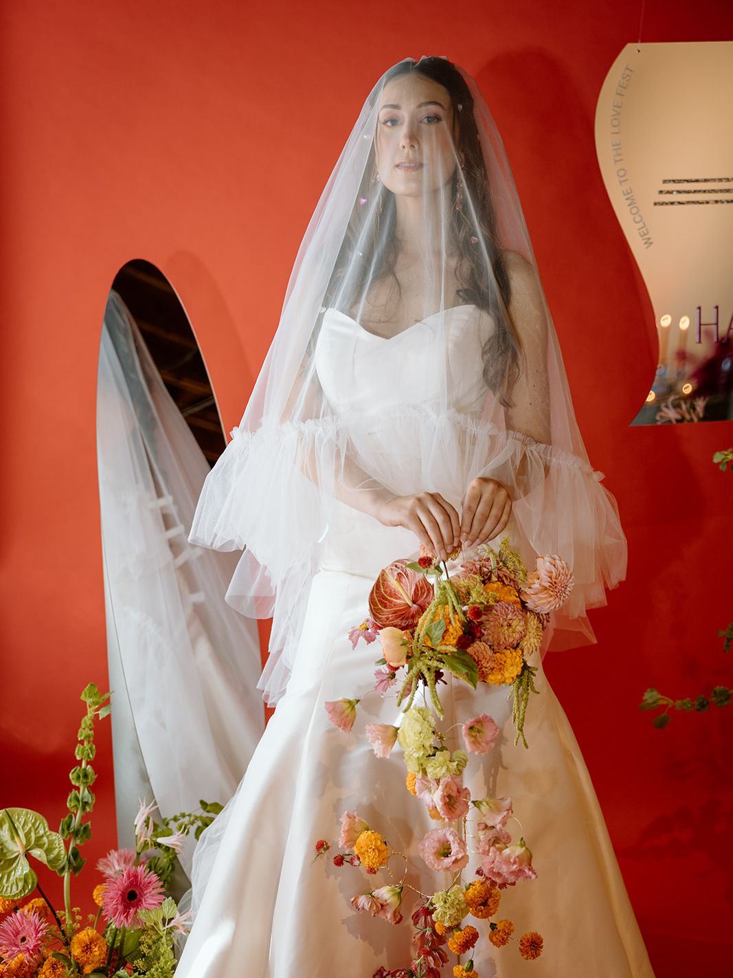 Bride in a modern white wedding gown and tiered blusher veil holding a cascading pink, orange and green floral bouquet.