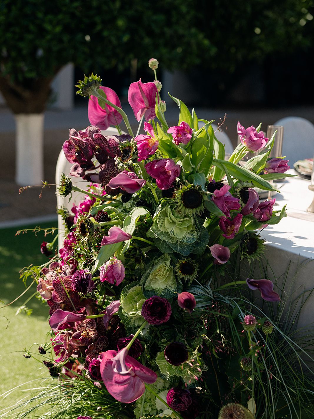 Close-up of a vibrant wedding floral installation with pink anthuriums, purple blooms, ornamental cabbage and textured greenery