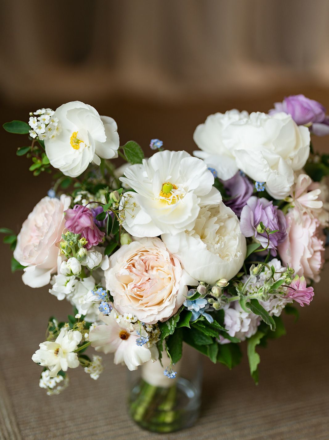 Loose wedding bouquet of white and blush flowers with lavender accents in a clear glass vase