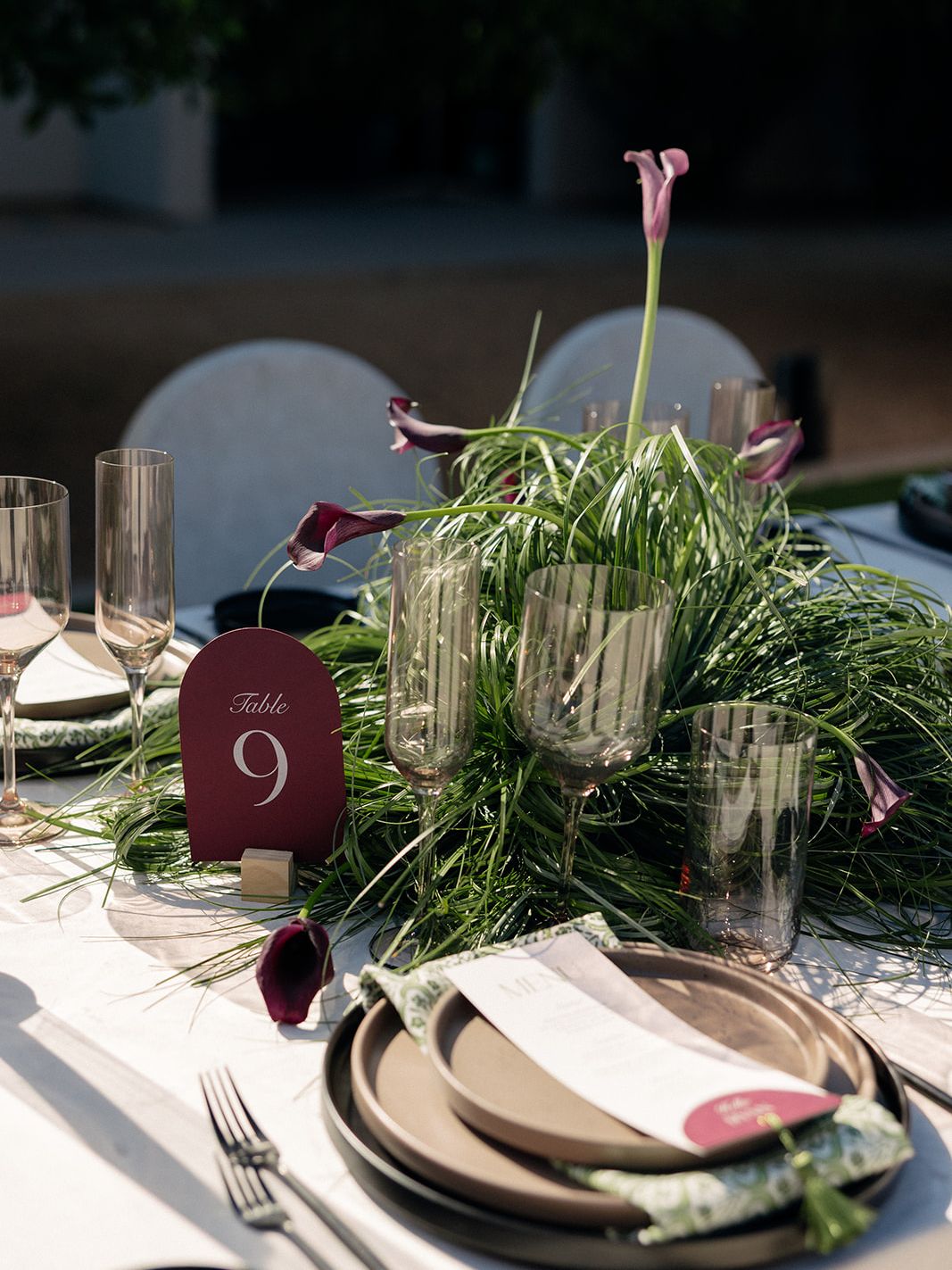 Modern wedding tablescape with wispy grasses, purple calla lilies, smoky glassware and a burgundy table number