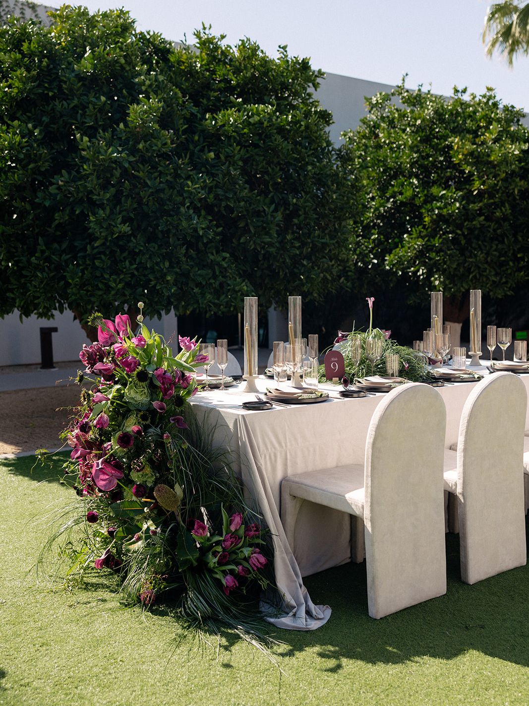 Outdoor wedding reception table featuring a lush cascading floral installation, modern place settings and tall glass candle holders