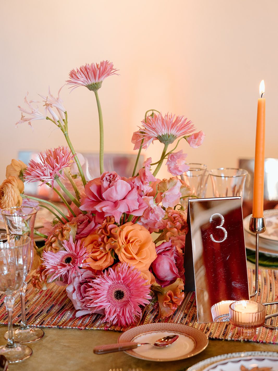 Pink and orange wedding centerpiece with sculptural florals, mirrored table number and orange taper candle