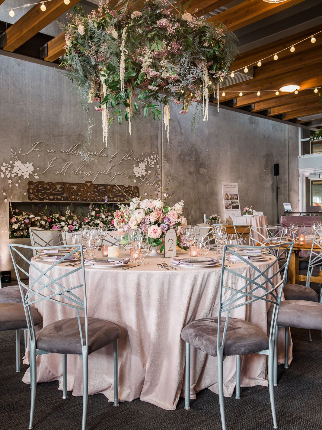 Wedding reception table with a pink floral centerpiece beneath a large suspended arrangement of flowers and greenery