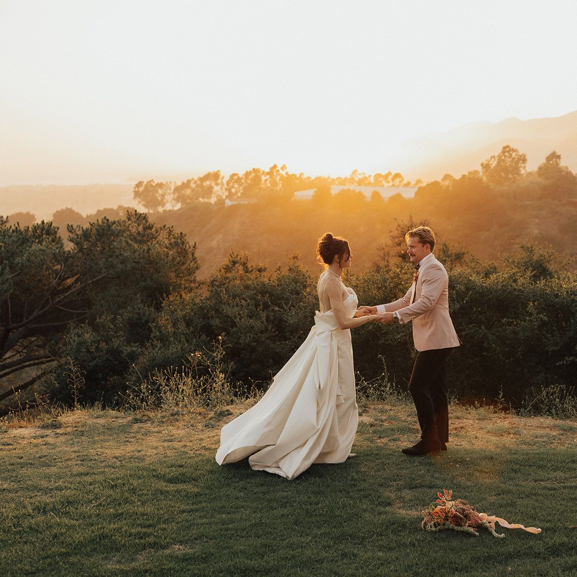 Bride and groom stand in golden hour glow against scenic vista 