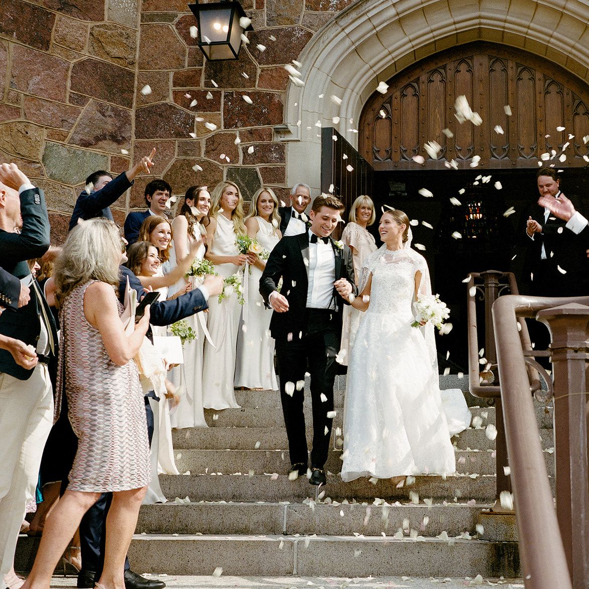 Isabel and John descend the staircase after ceremony t Plymouth Congregational Church as petals waft through the air
