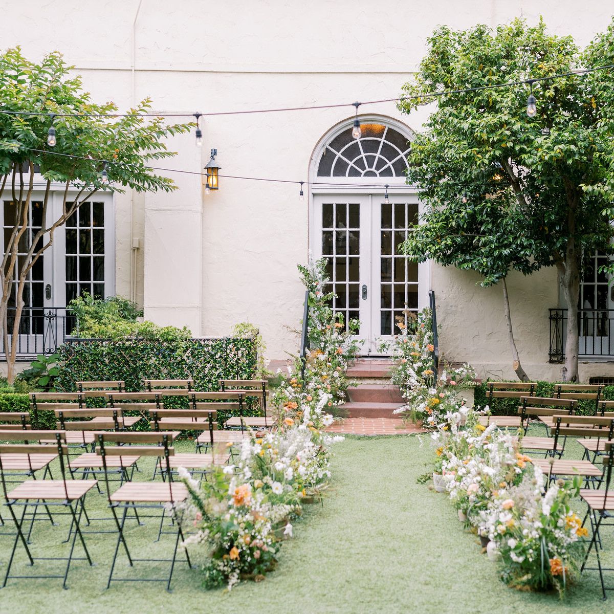 Wedding aisle and chairs and florals in front of a large window and tree