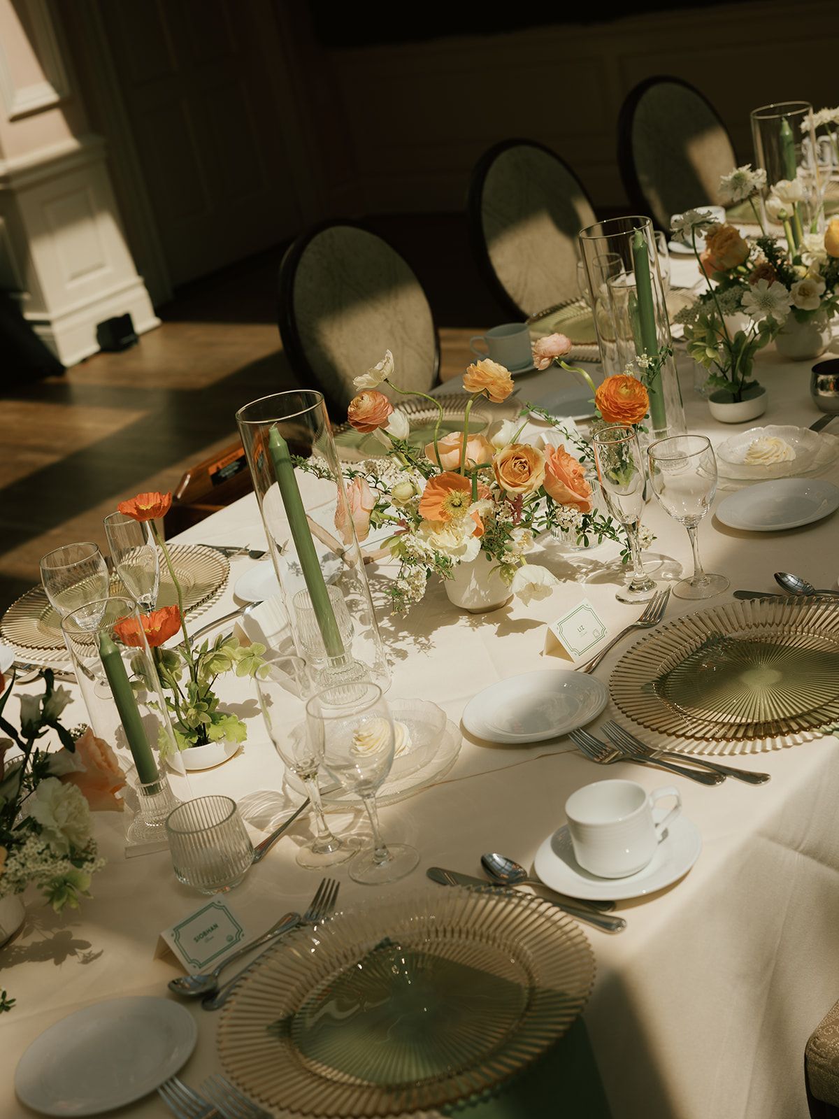 Wedding reception table set with glassware, gold chargers, white place settings and peach-and-white floral arrangements.