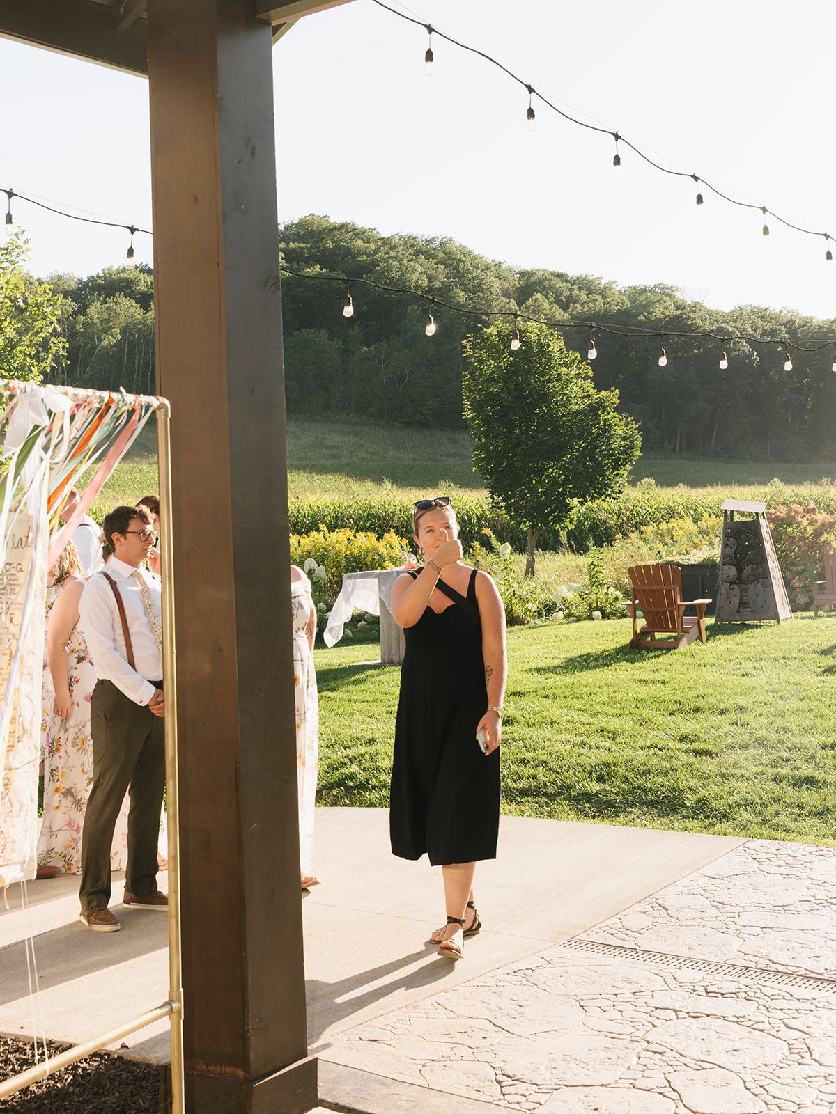 Guests gather beneath string lights at an outdoor wedding reception beside a colorful ceremony installation.