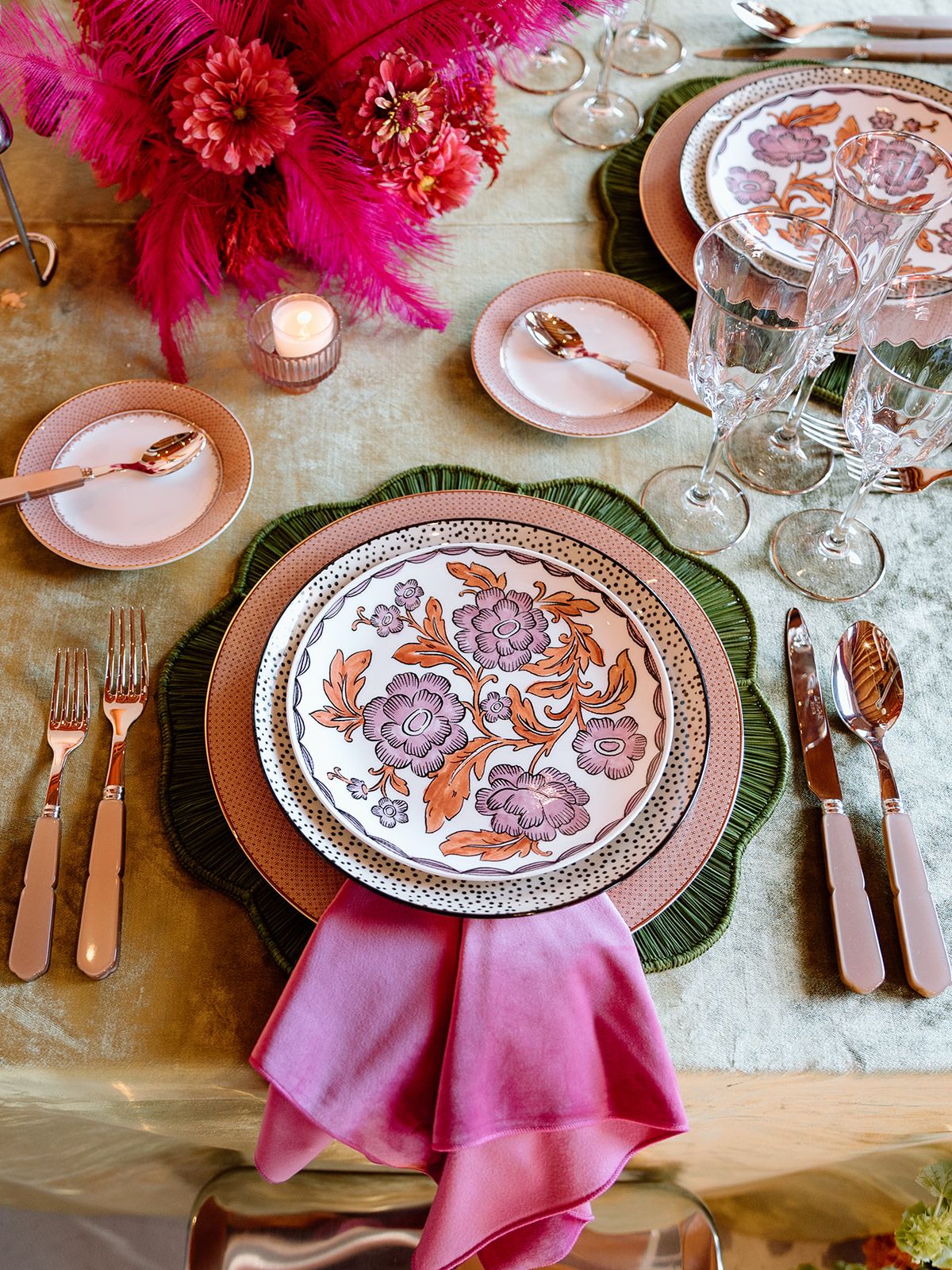Maximalist wedding place setting with floral-patterned china, green charger, pink napkin, crystal glassware and colorful florals