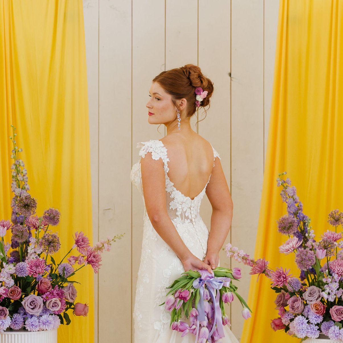 Model poses at altar with yellow fabric structures and lavender florals