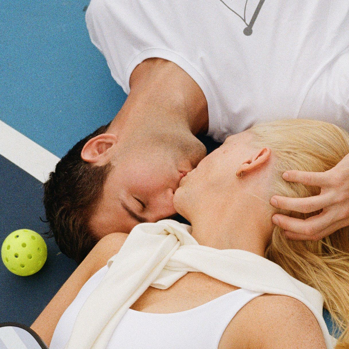 Jennifer and Sean lay on the pickleball court and share a kiss