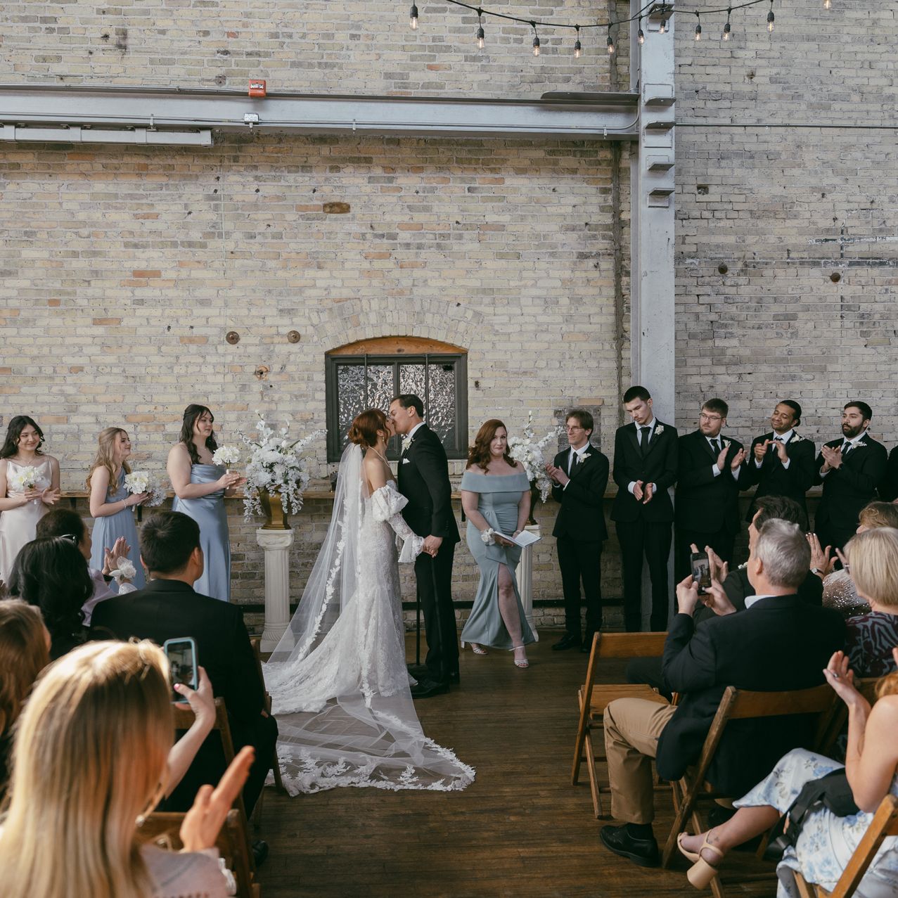 Bride and groom stand at the altar with bridal party framing them against the industrial interior of The Cooperage