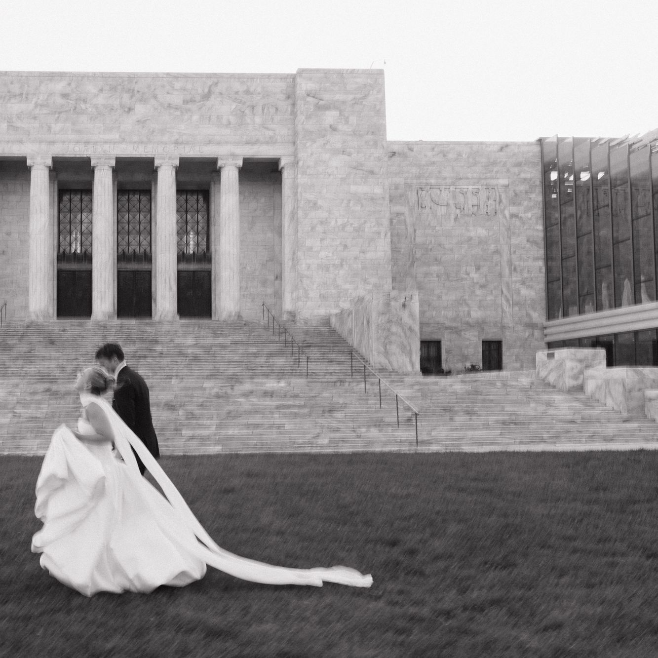 Bride and groom walk outside of The Joslyn art museum on their wedding day, in black and white