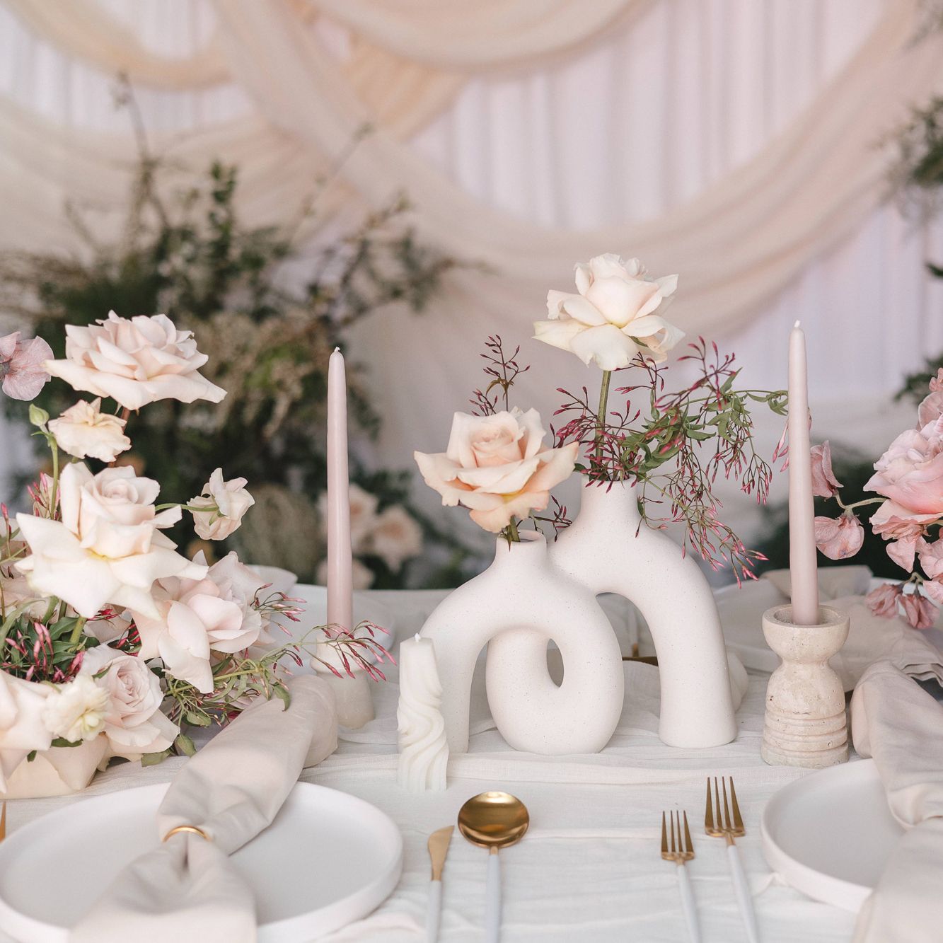 Tablescape featuring rosy hues and sculptural stone vases in imagined reception