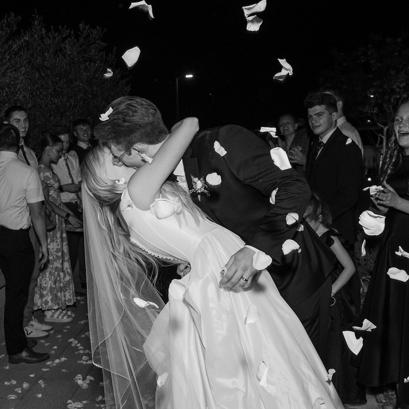 Bride and groom share a celebratory kiss while rose petals rain over them in wedding day at a family farm