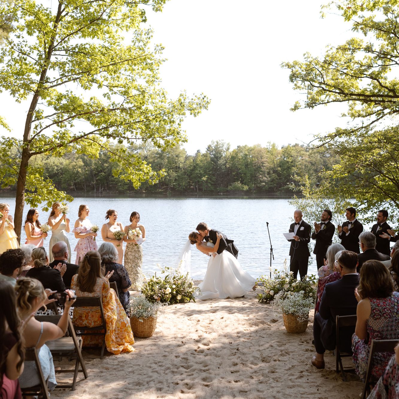 Molly and Ralph kiss at the altar in their outdoor ceremony framed by trees and their loved ones at Camp Elsewhere