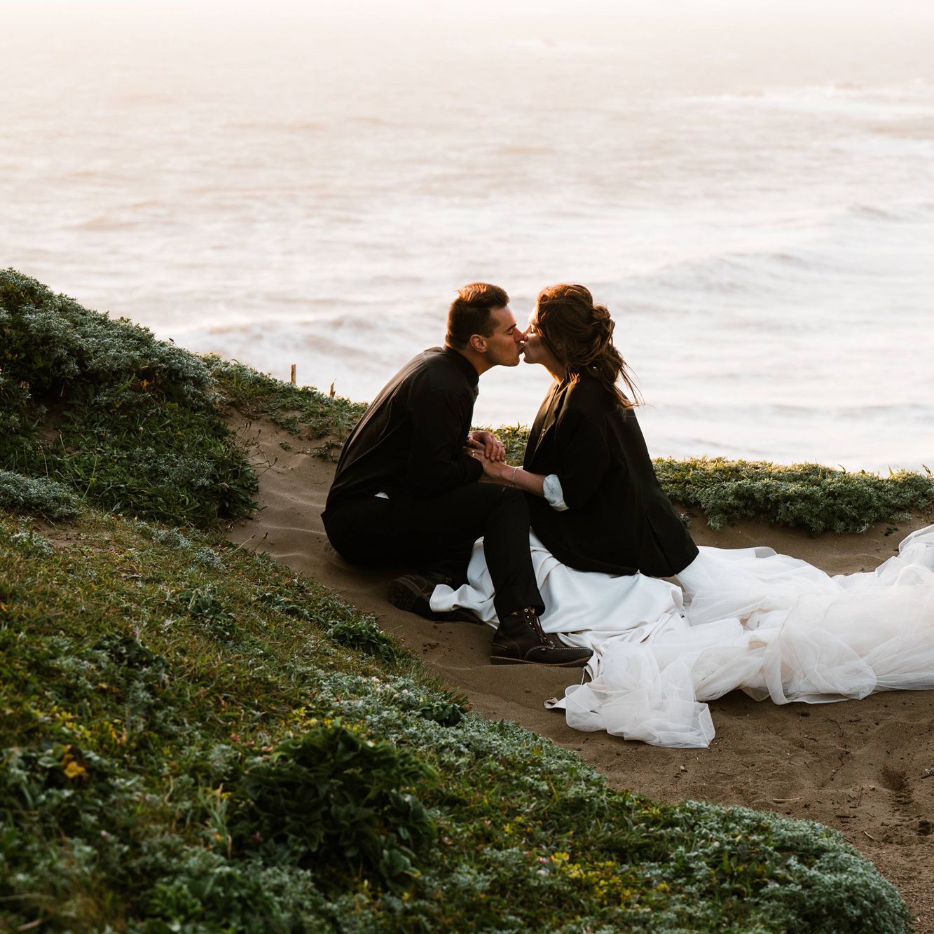 Olivia and Brian sit and share a kiss during their wedding day portraits on the southern coast of Oregon