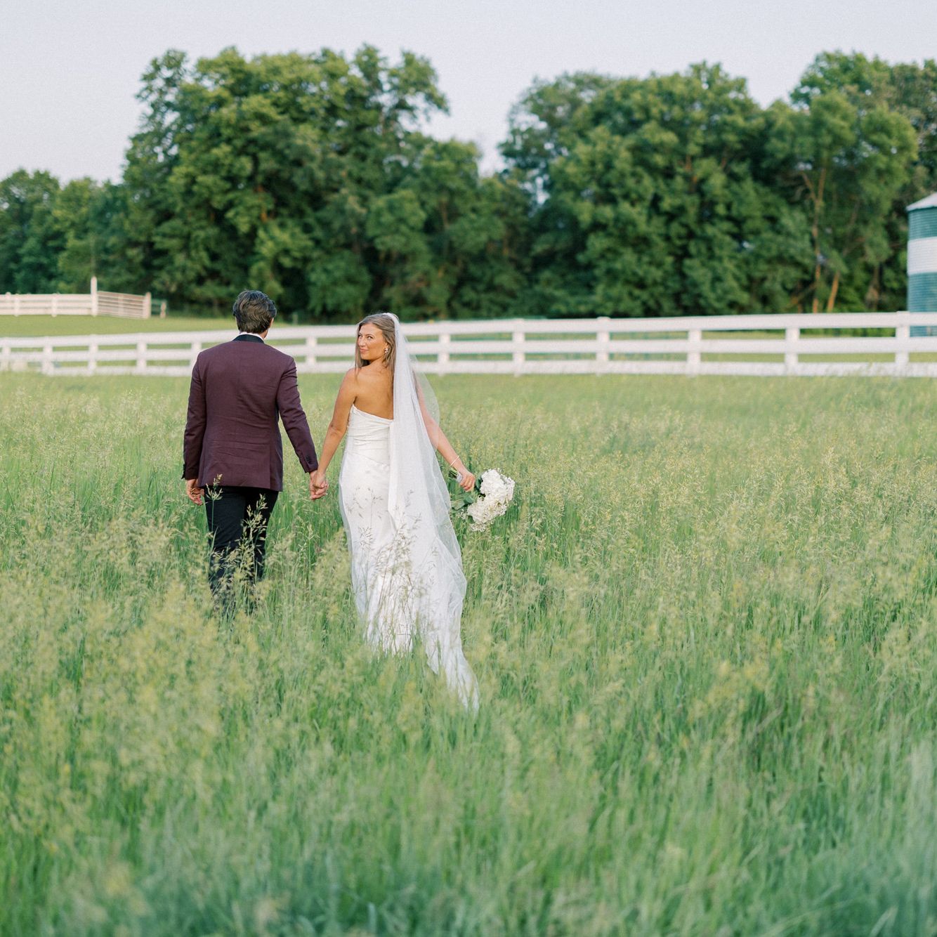 Bride and groom hold hands walking through the field of a private estate