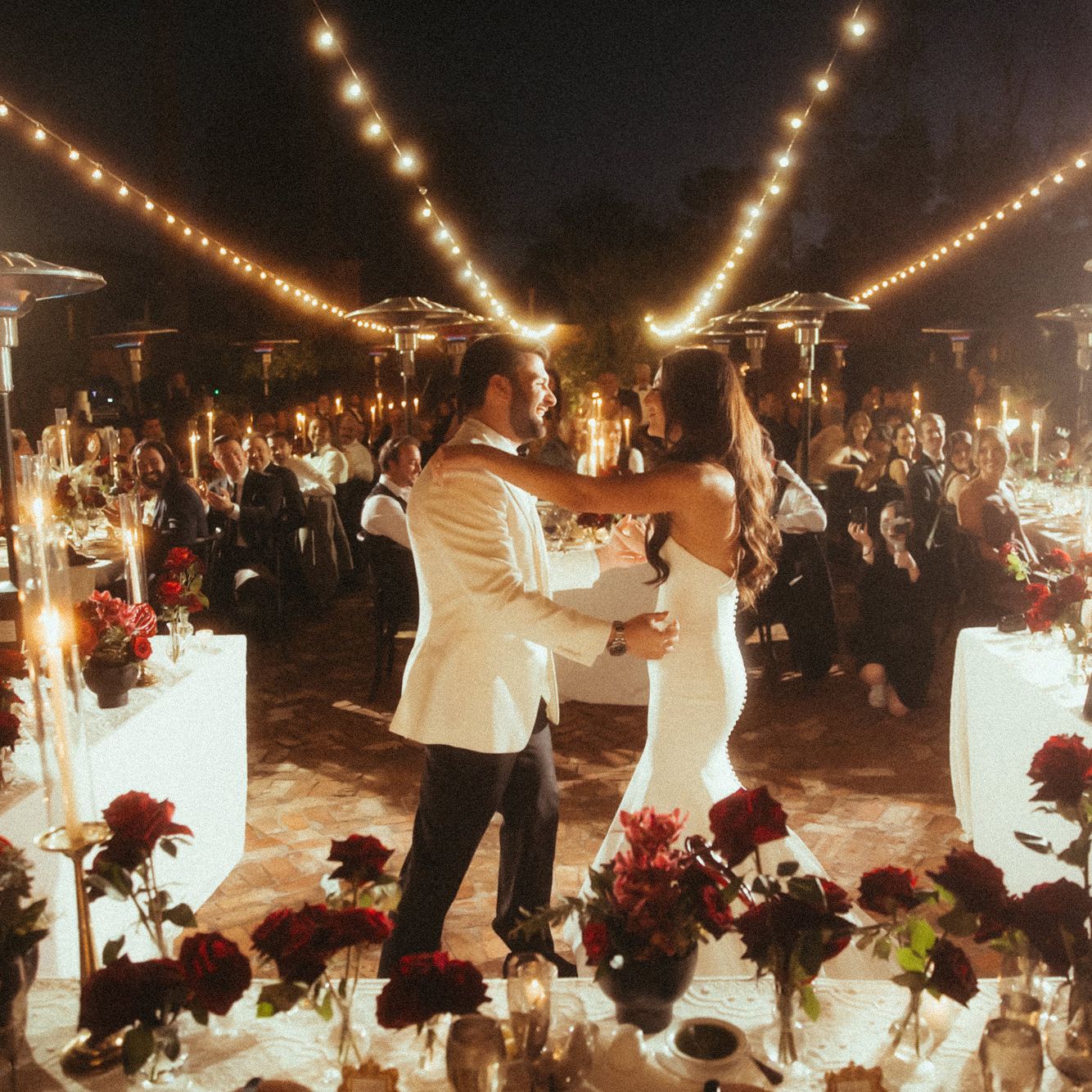 Bride and groom share a dance framed by their candlelit outdoor reception featuring bold red flowers at Royal Palms Resort and Spa
