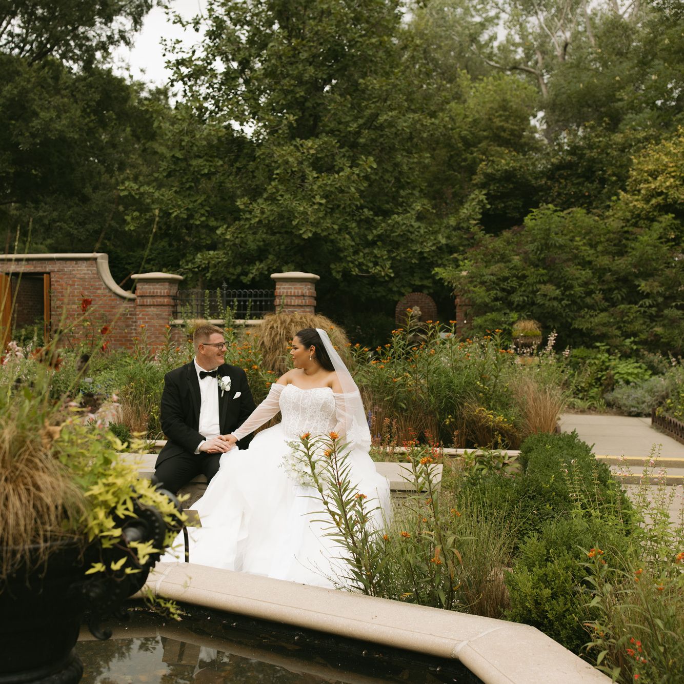 Gali and trevor sit on a bench in their wedding attire