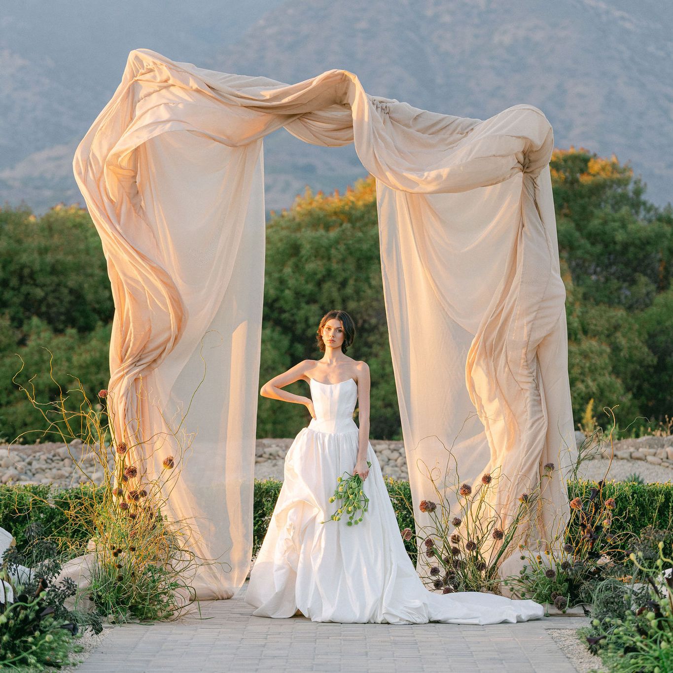 Model poses under architectural and organic altar against mountainous landscape at Topa Vista