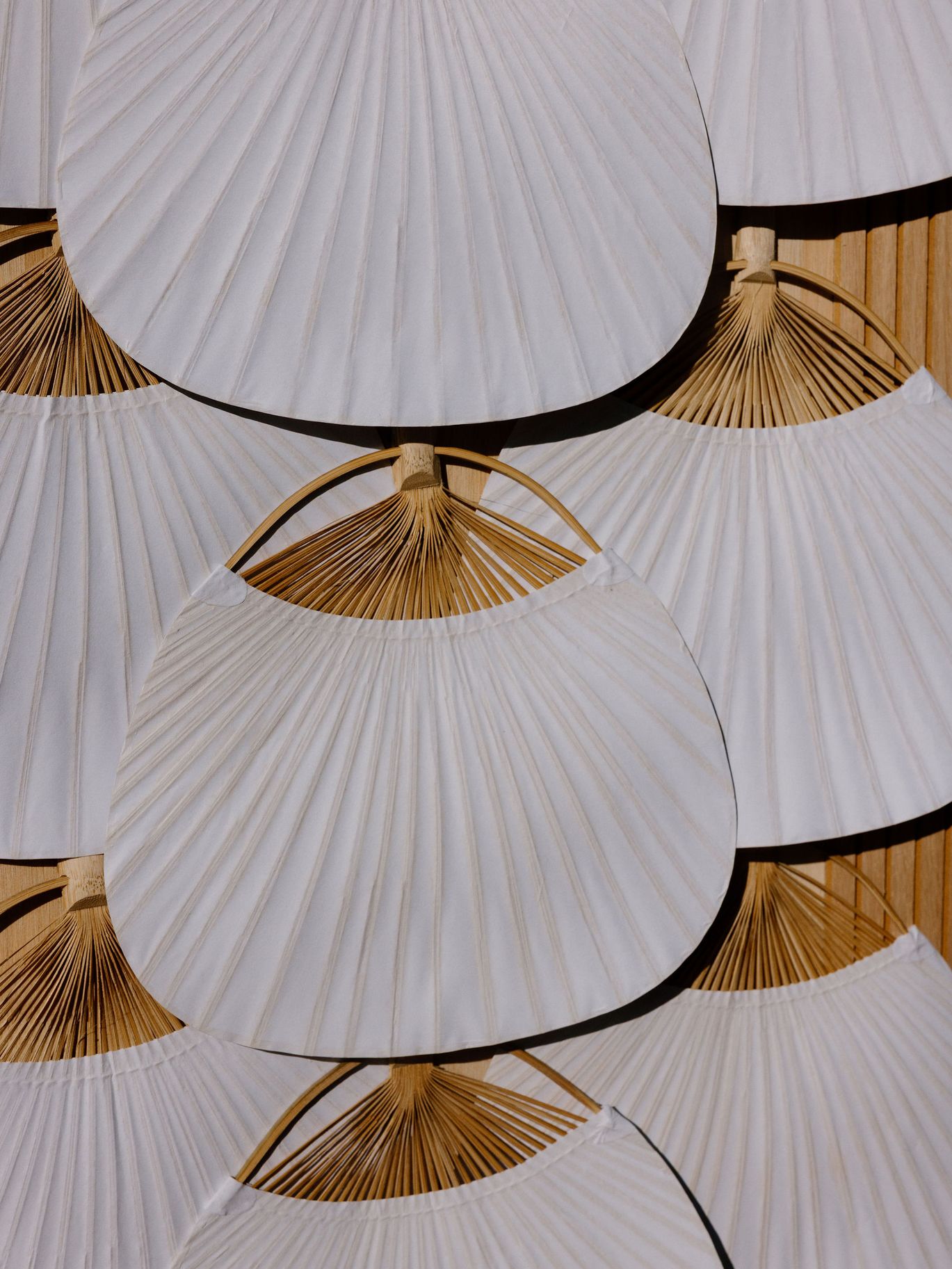 Close-up of layered white folding fans with natural wood handles used as part of a wedding escort card display