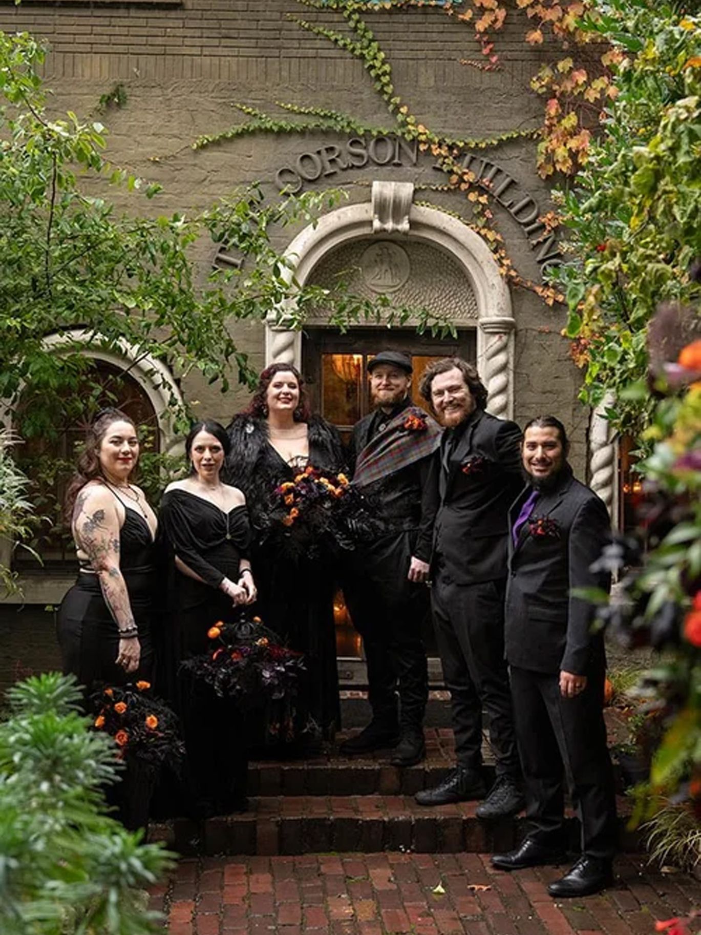 Paige and Dylan pose with their wedding party outside The Corson Building, whose entrance is decorated for Halloween.
