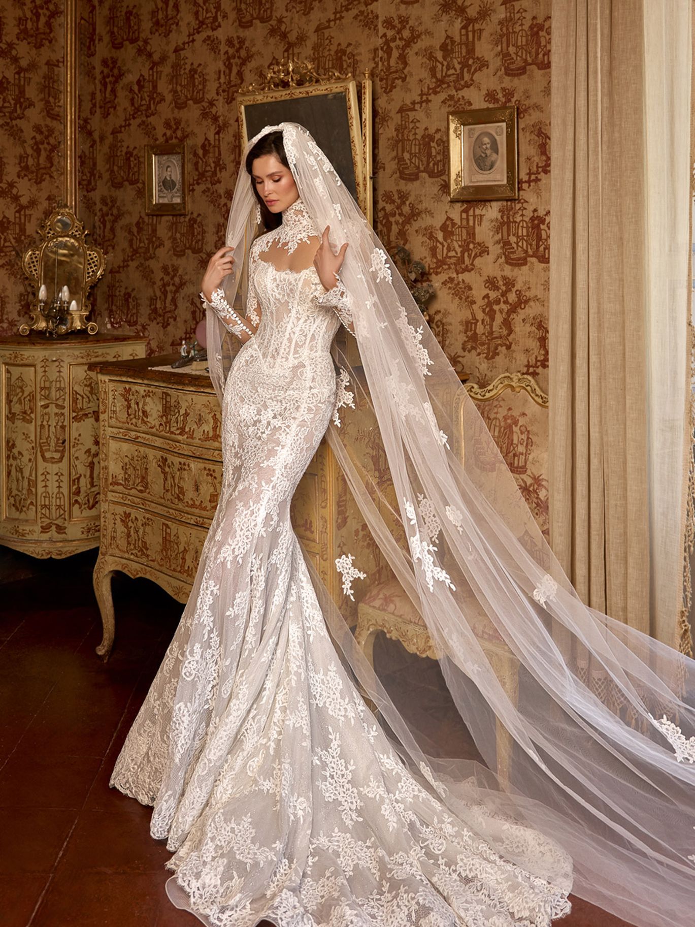 Oksana Mukha Damira wedding gown from the Fall 2027 Lumière Heritage collection, featuring a high lace neckline, long sleeves and a fitted floral lace silhouette.