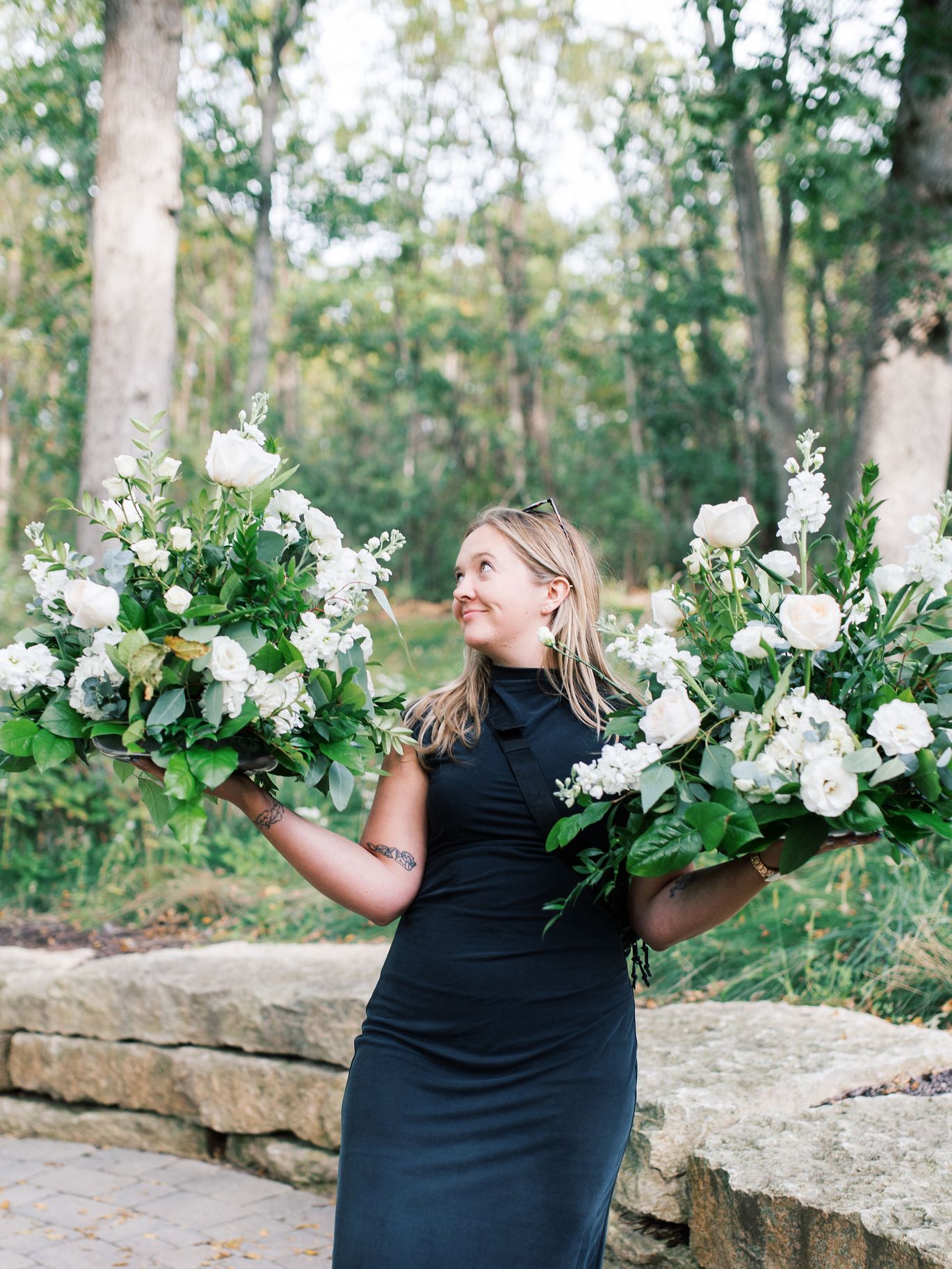 Lydia Turino, founder and lead planner of Miriam Events Co., holds white floral arrangements among greenery in a garden.