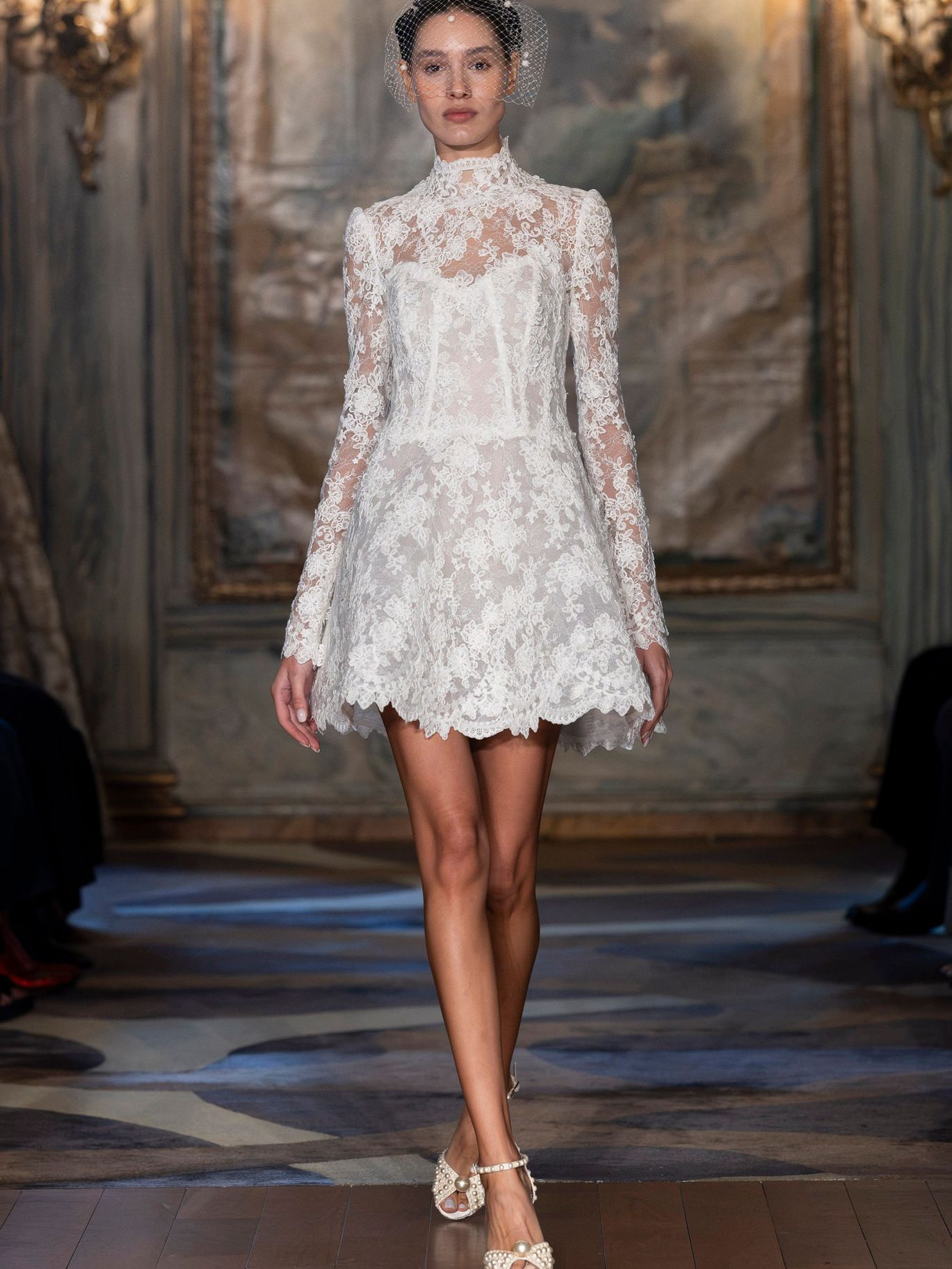 Sareh Nouri The Last Dance mini wedding dress from the Fall 2027 collection, featuring a high neckline, long sleeves, Alençon lace and scalloped hem.