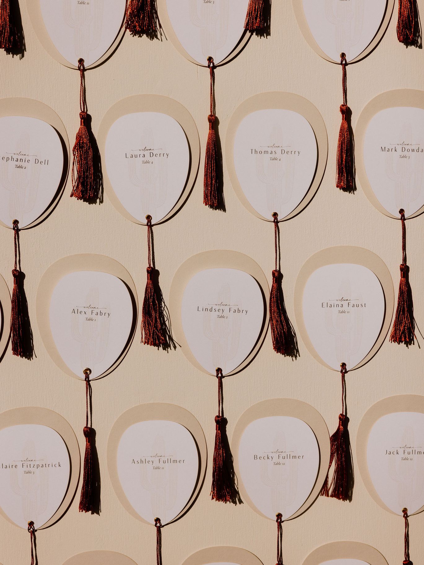 Close-up of white wedding escort cards displaying guest names and table numbers with rust-colored tassels