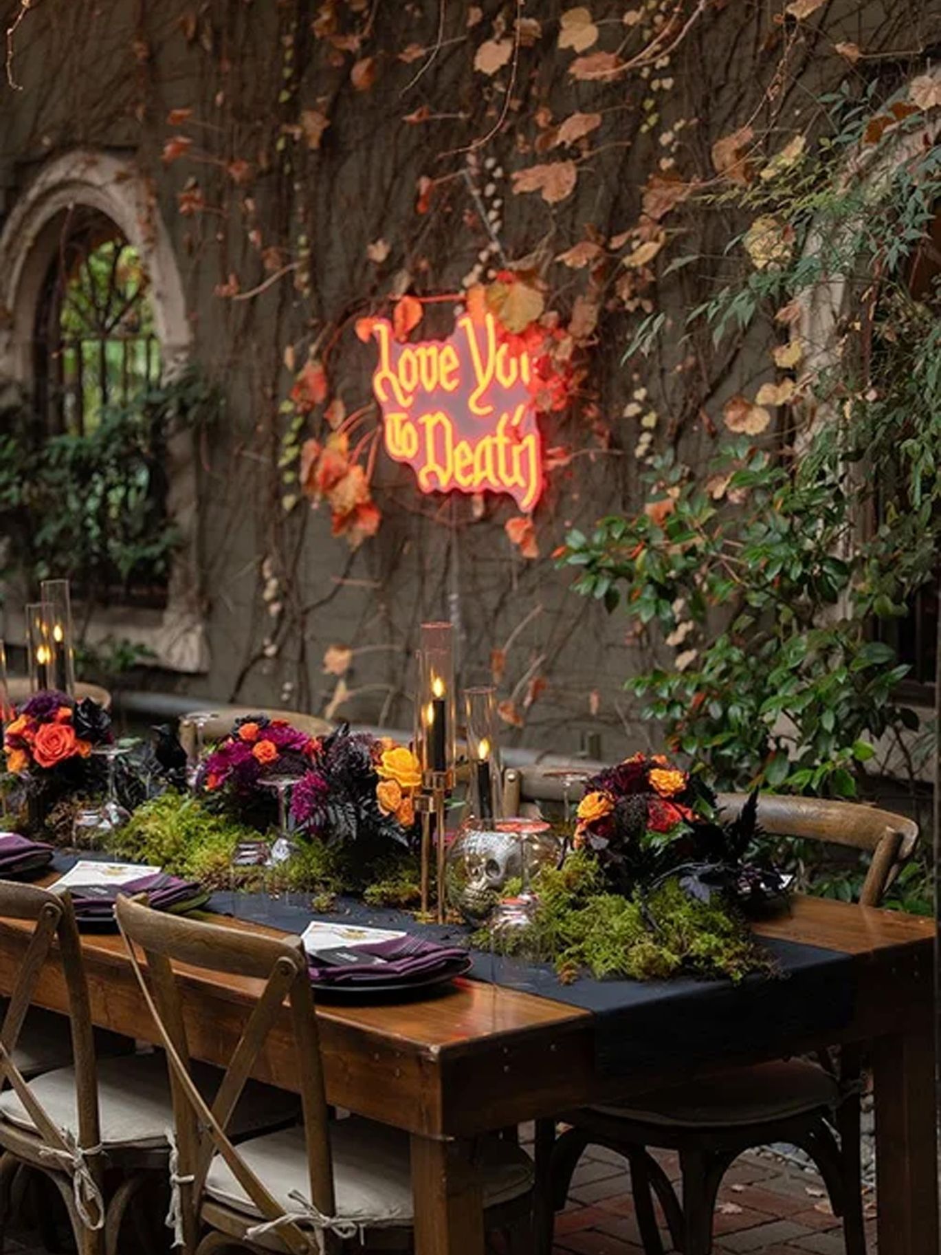 A glowing “Love You to Death” sign hangs above a floral reception table at the couple’s Halloween wedding.