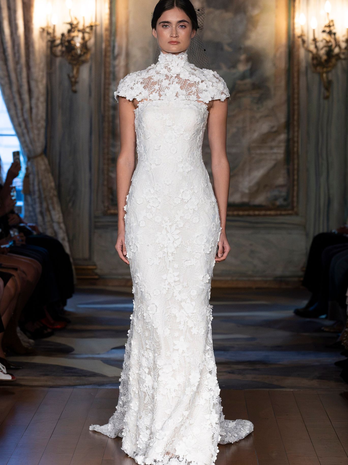 Sareh Nouri Estelle wedding gown from the Fall 2027 bridal collection, featuring three-dimensional floral lace, a fitted silhouette and matching high-neck lace capelet.