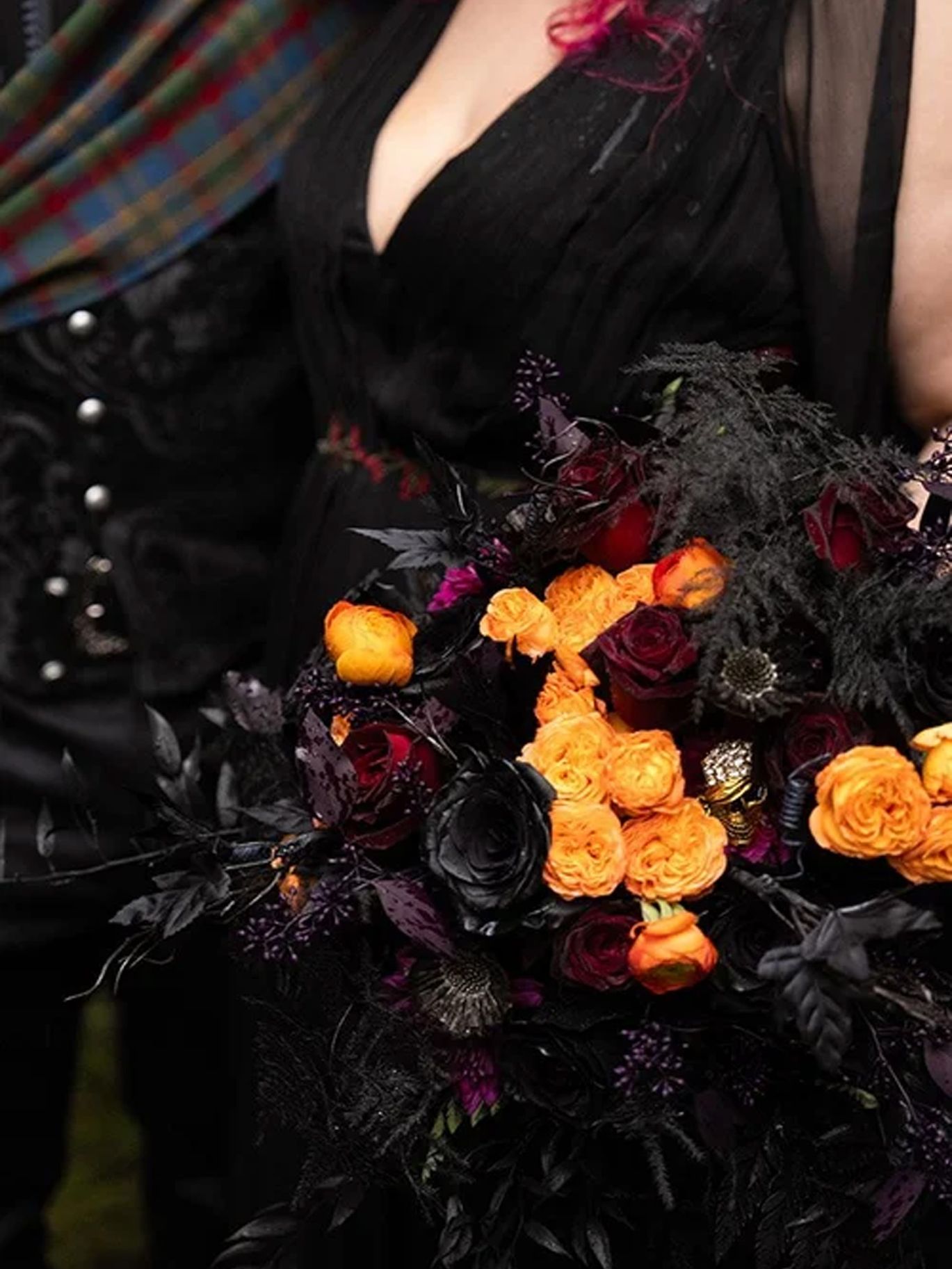 A Halloween wedding bouquet of orange and dark red roses, black foliage and purple accents complements the bride’s black gown.