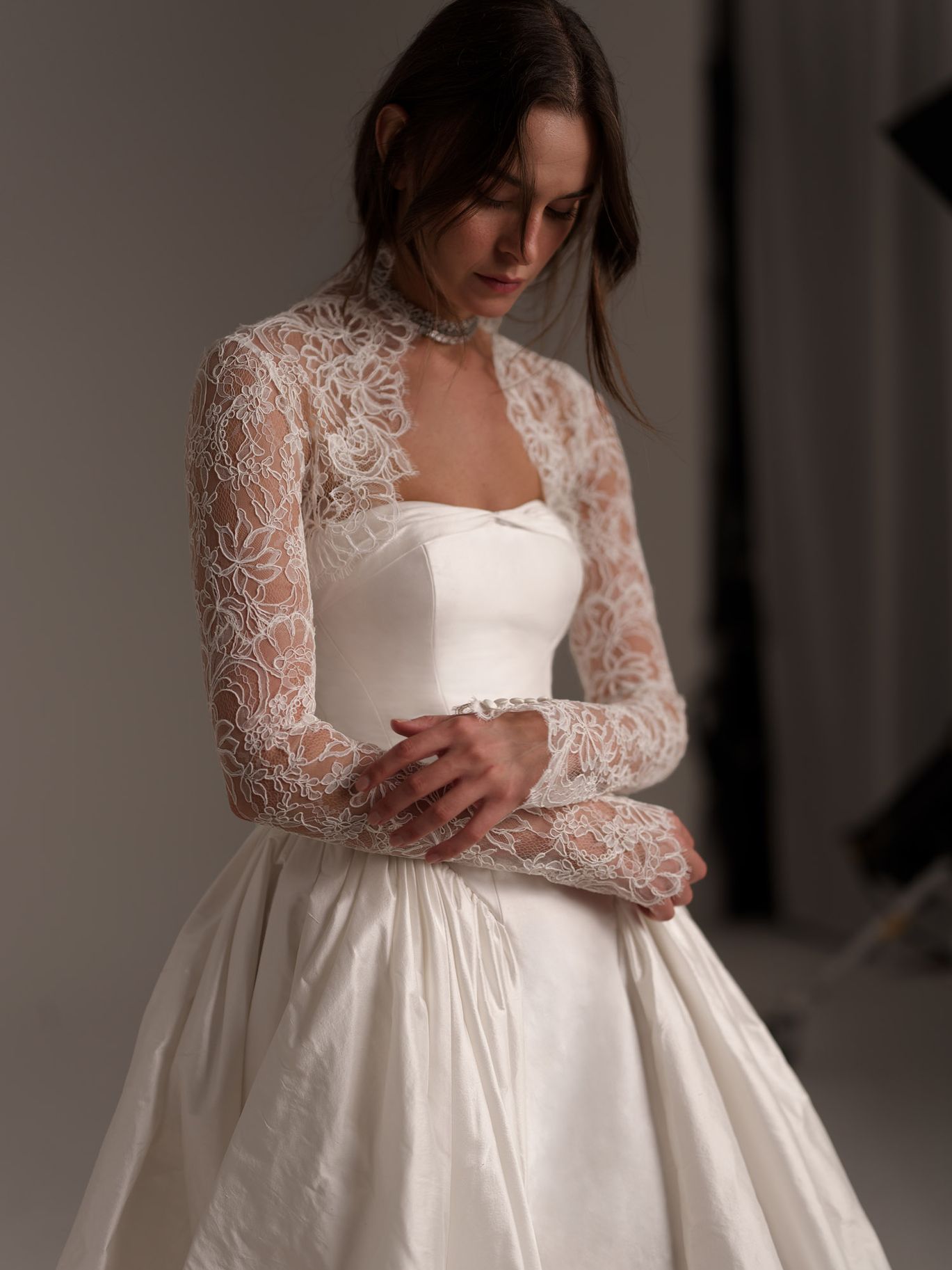 Lihi Hod Nelly Topper from the Fall 2027 bridal collection, featuring sheer floral lace, a high neckline and long sleeves over a strapless wedding gown.