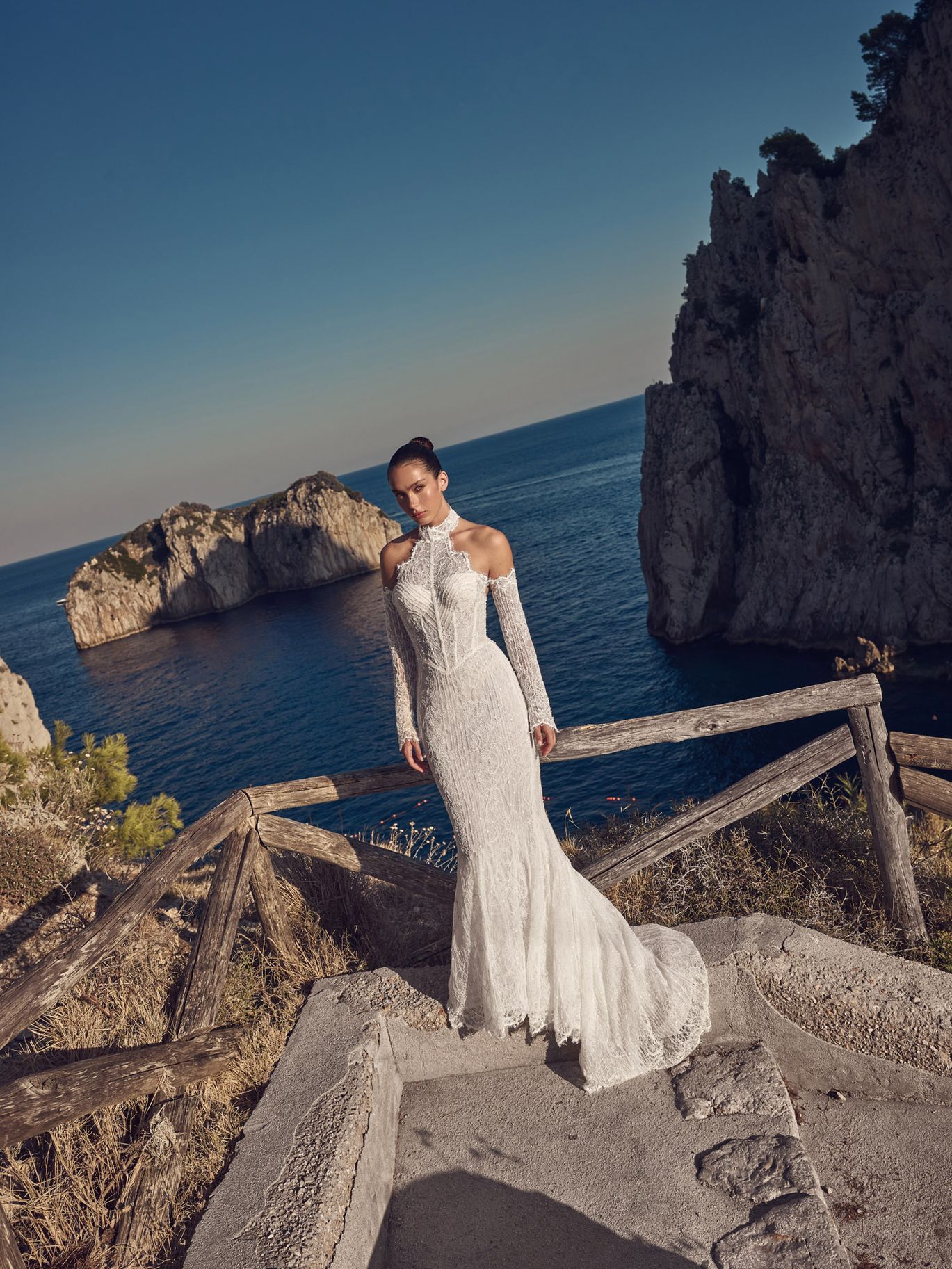 Ricca Sposa Couture Fall 2027 Couture Capri wedding gown featuring a high lace collar, open shoulders, detached lace sleeves and a fitted skirt.