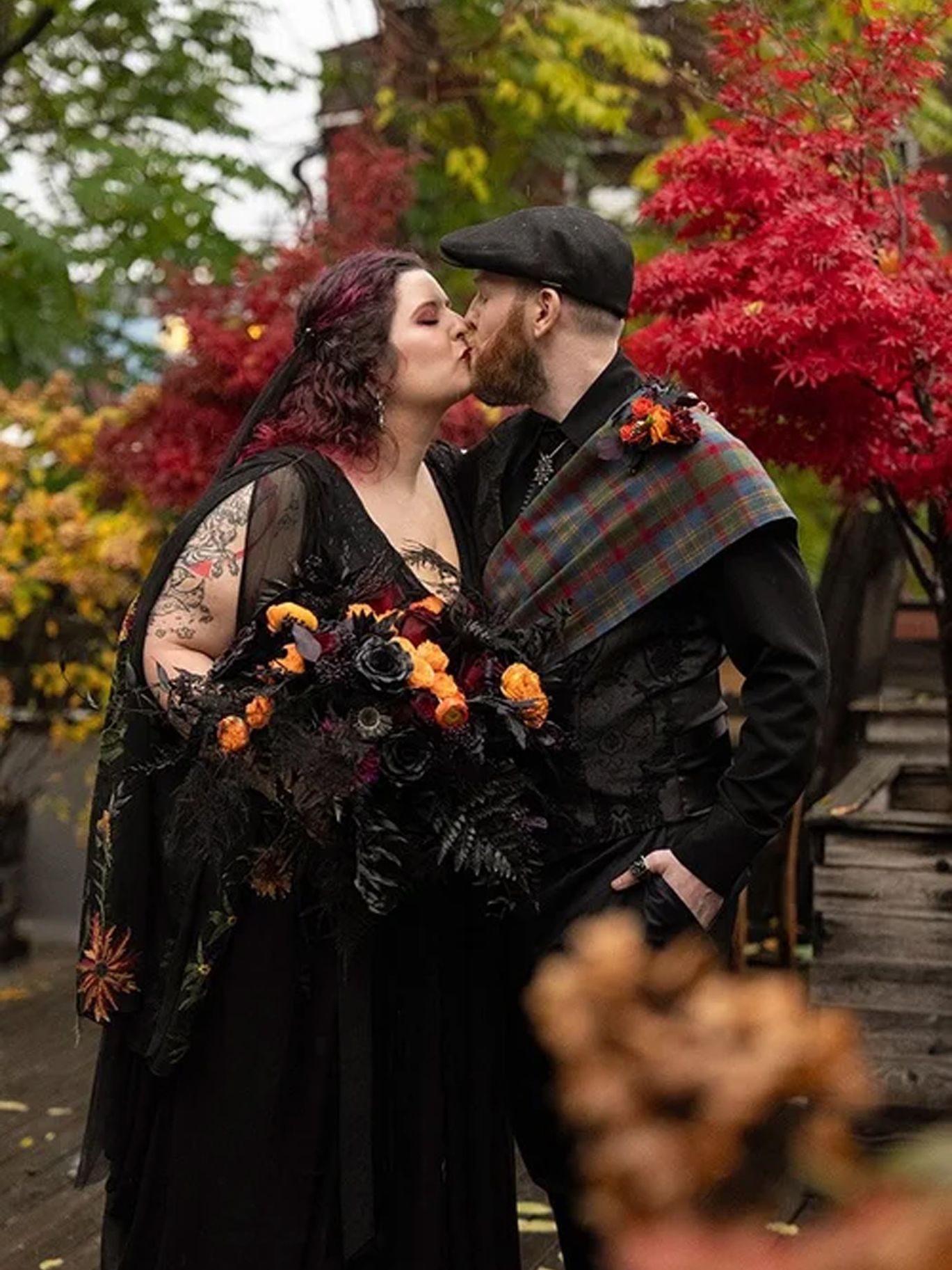 Paige and Dylan kiss beneath autumn leaves during portraits for their Halloween wedding in Seattle.