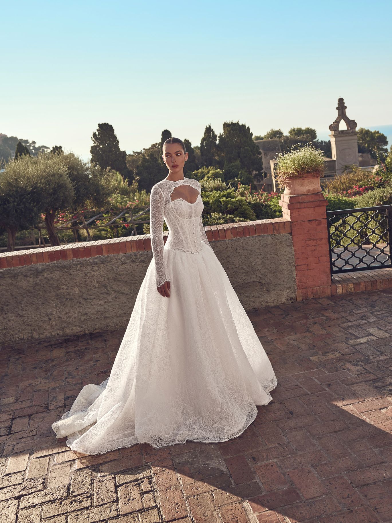 Ricca Sposa Couture Fall 2027 Couture Capri ballgown featuring a high-neck lace overlay, sheer long sleeves, structured corset and full skirt.