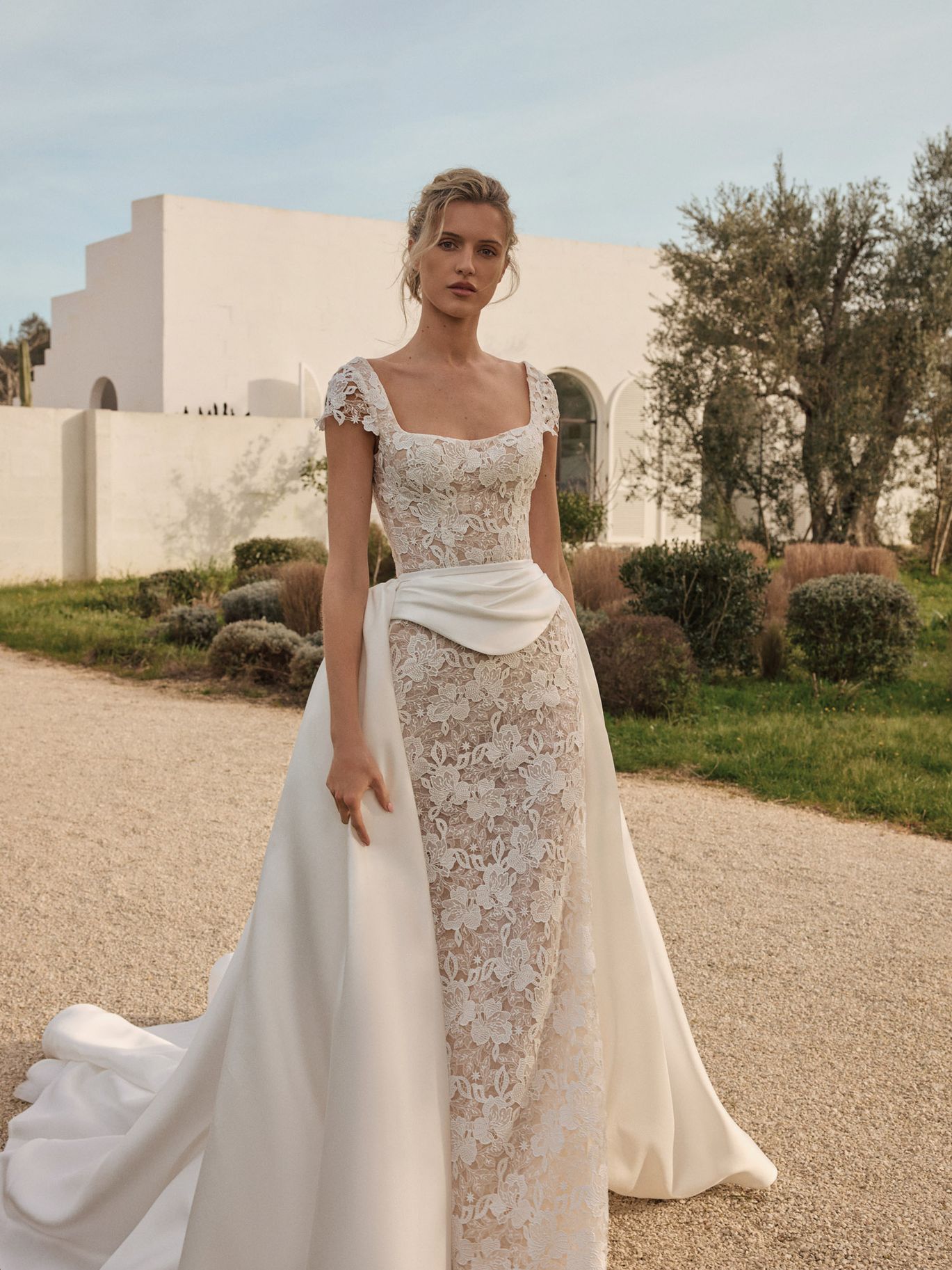 Eva Lendel Seraphine lace wedding dress with cap sleeves and a softly draped overskirt at the waist, featured in a romantic draping trend roundup from New York Bridal Fashion Week.
