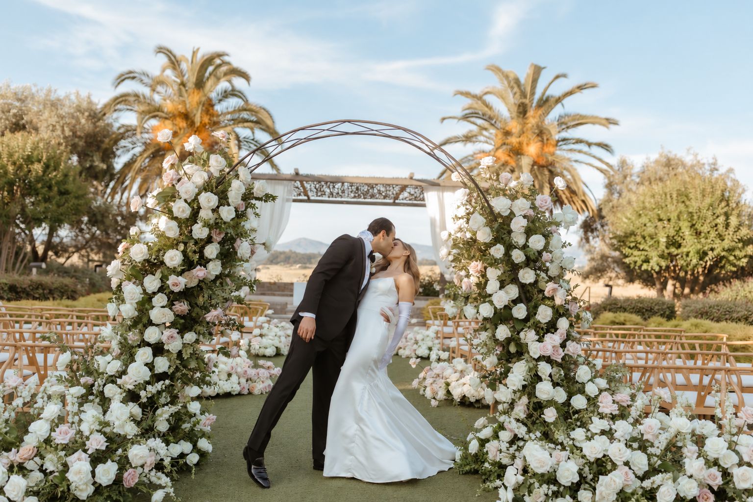 Kissing newlyweds beneath a floral arch Carnreros Resort Blissful Events.png