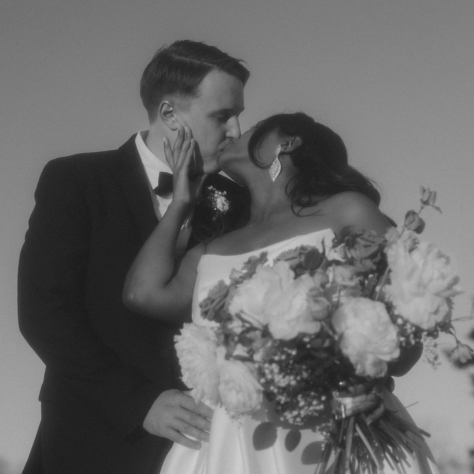 Tsion and Ben kiss in their wedding attire while showing Tsion's bouquet or peonies. 